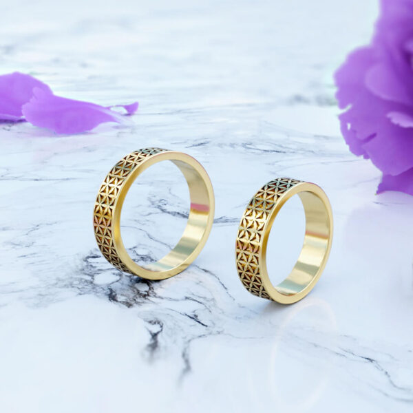 Anillos modelo flor de la vida de matrimonio en oro de 18k en posición vertical en fondo de flores